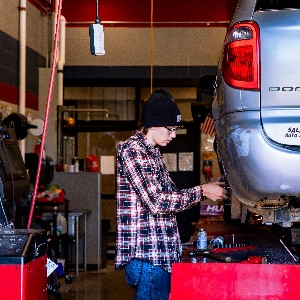 A student works on the rear wheel of a raised car.
